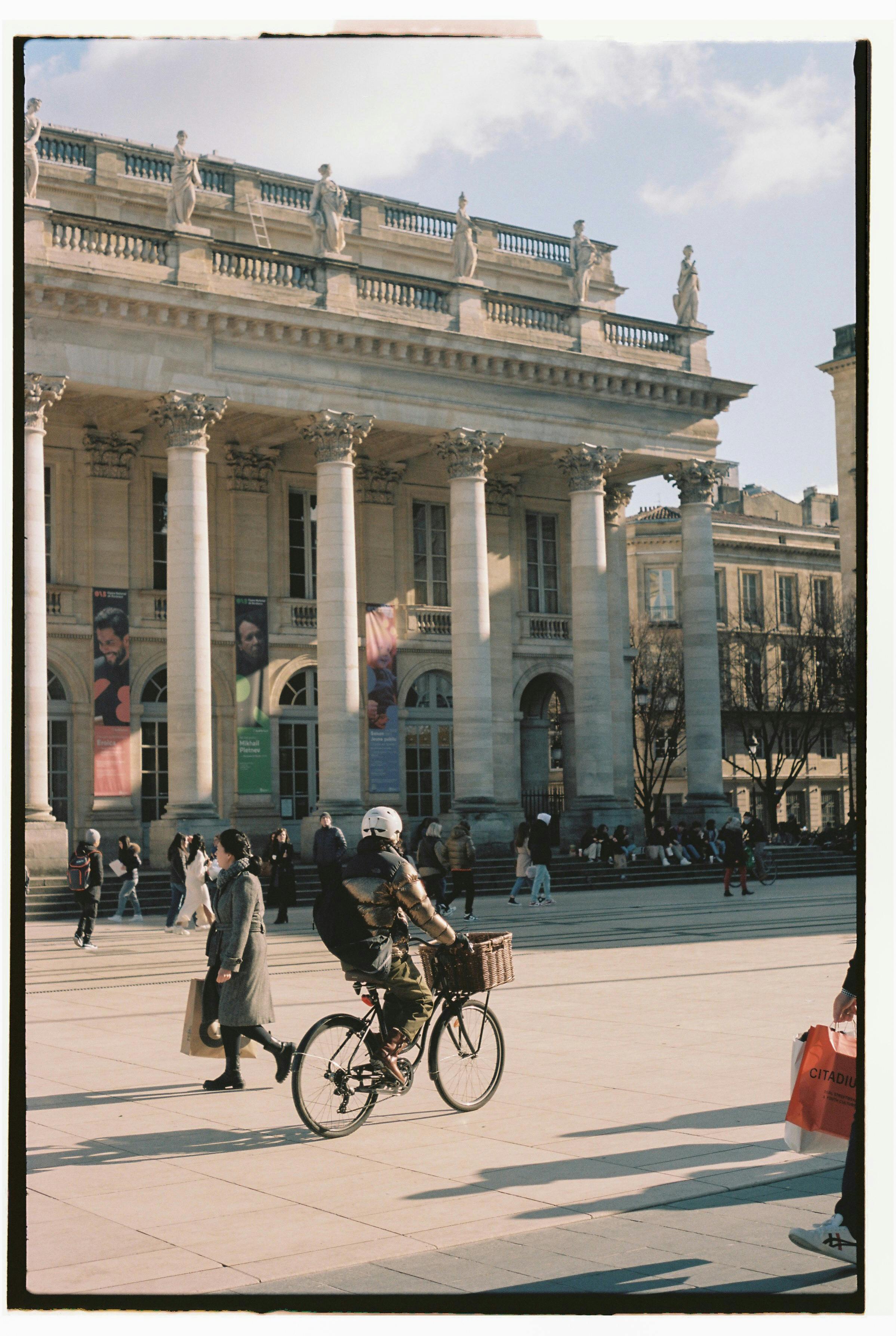 Cyclist rides past the historic Grand Theatre in Bordeaux on a sunny day.