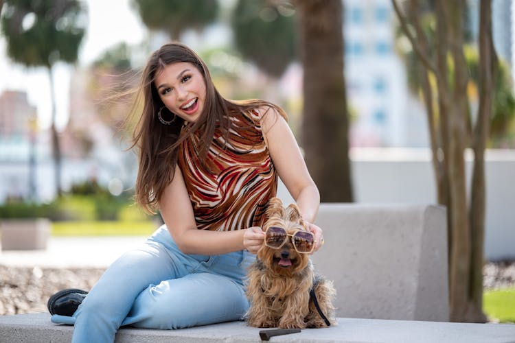 Laughing Woman Sitting On A Bench With Her Dog Wearing Sunglasses