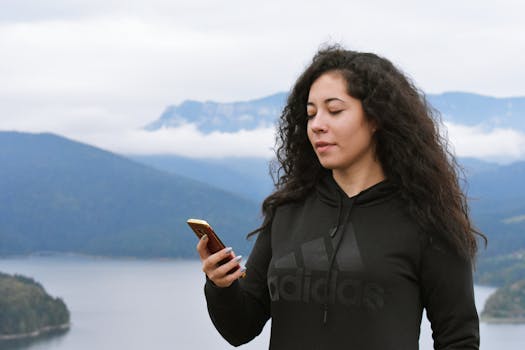 一位年轻女子在美丽的山水背景下使用手机，享受着宁静的户外生活