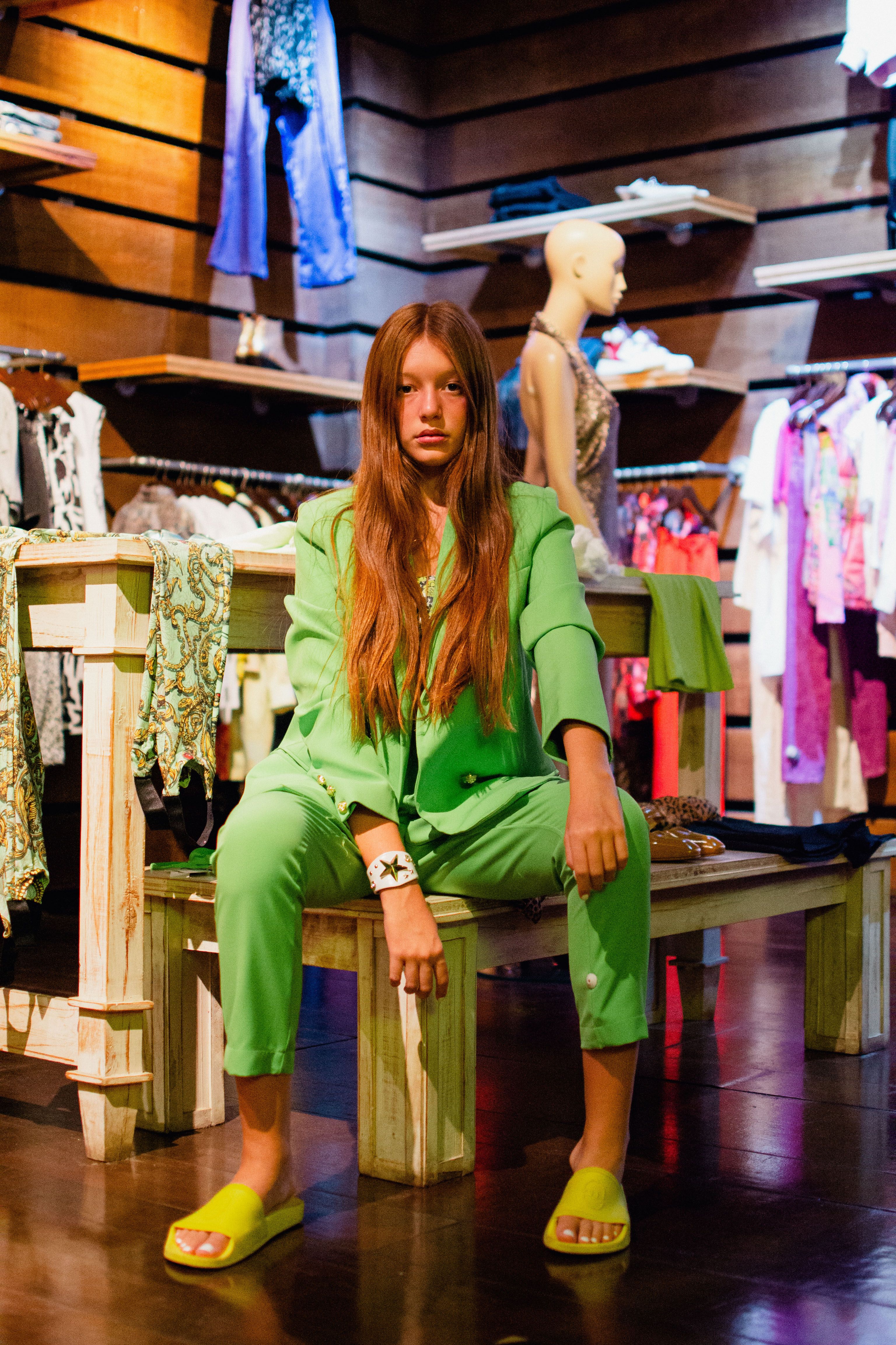 Mulher jovem em um traje verde vibrante posando com confiança em um ambiente de loja de moda contemporânea.