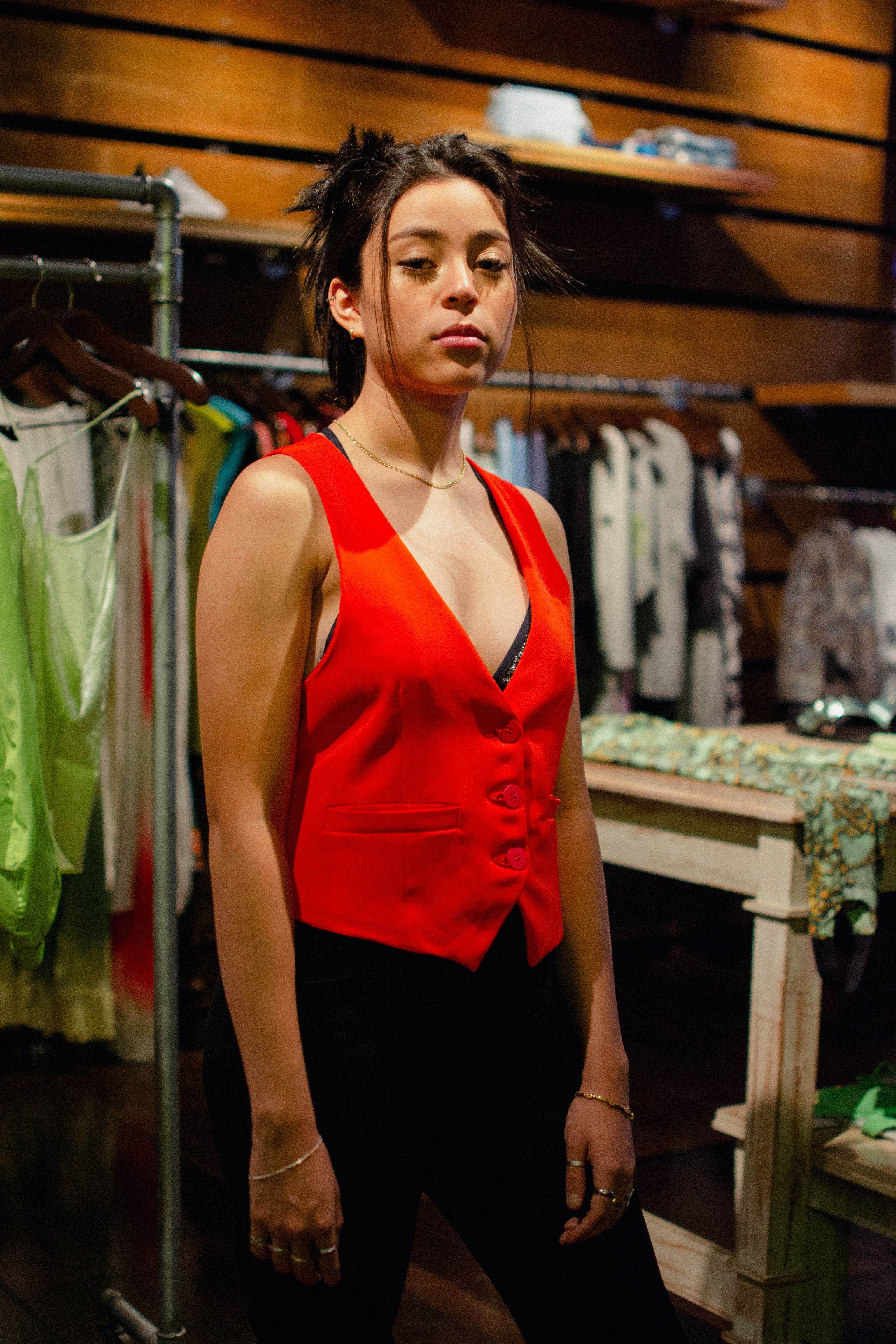 Fashionable young woman in a red vest poses confidently in a trendy clothing store setting.
