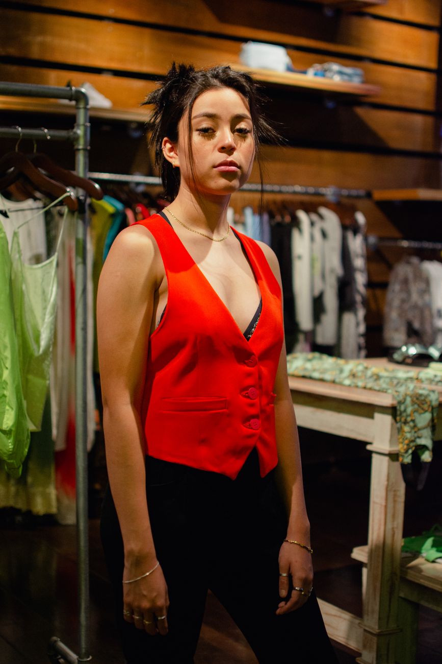 Fashionable young woman in a red vest poses confidently in a trendy clothing store setting.