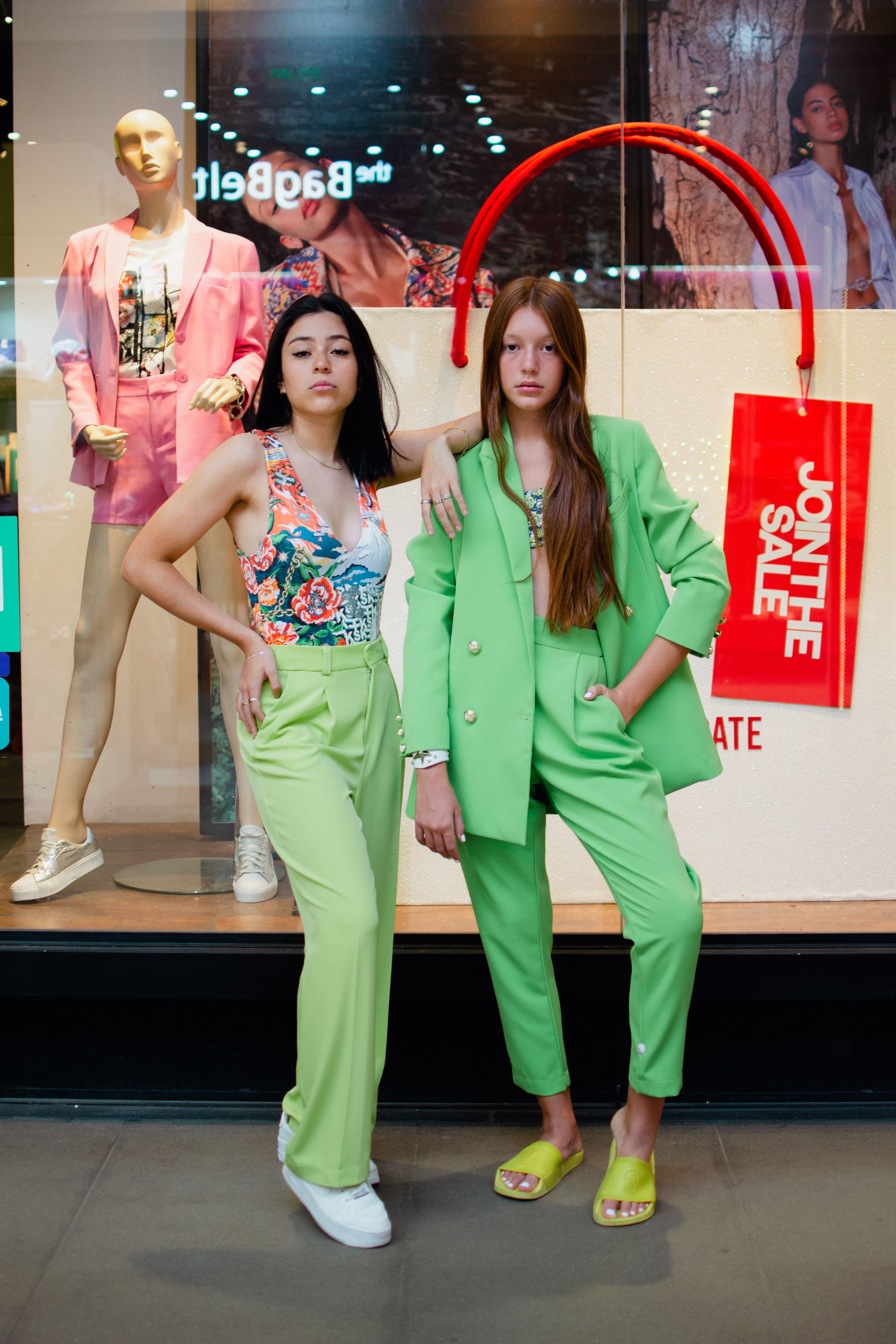 Duas mulheres elegantes em uma vitrine exibem trajes verdes estilosos e padrões florais.
