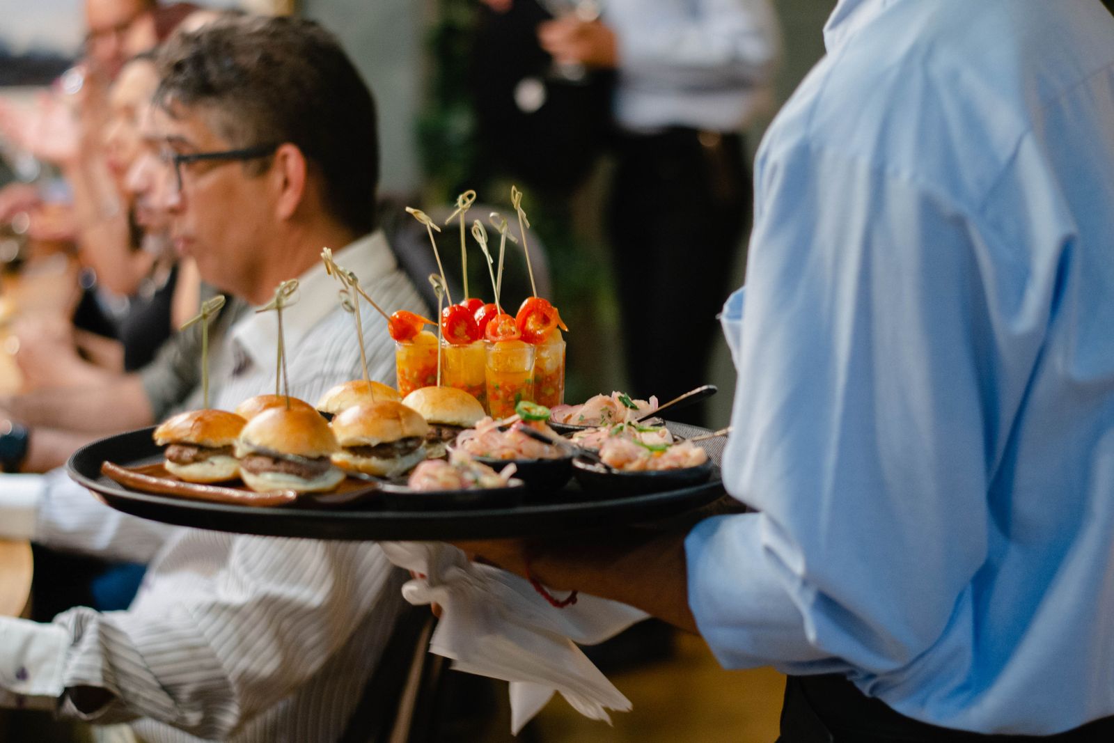 A server carrying a tray of sliders and canapés through a reception
