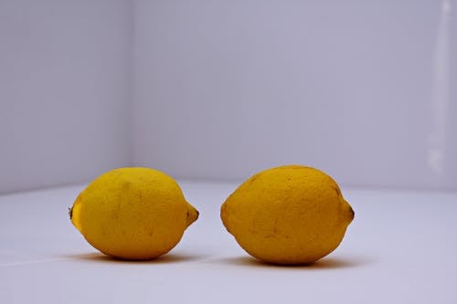 Два желтых лимона на белой поверхности