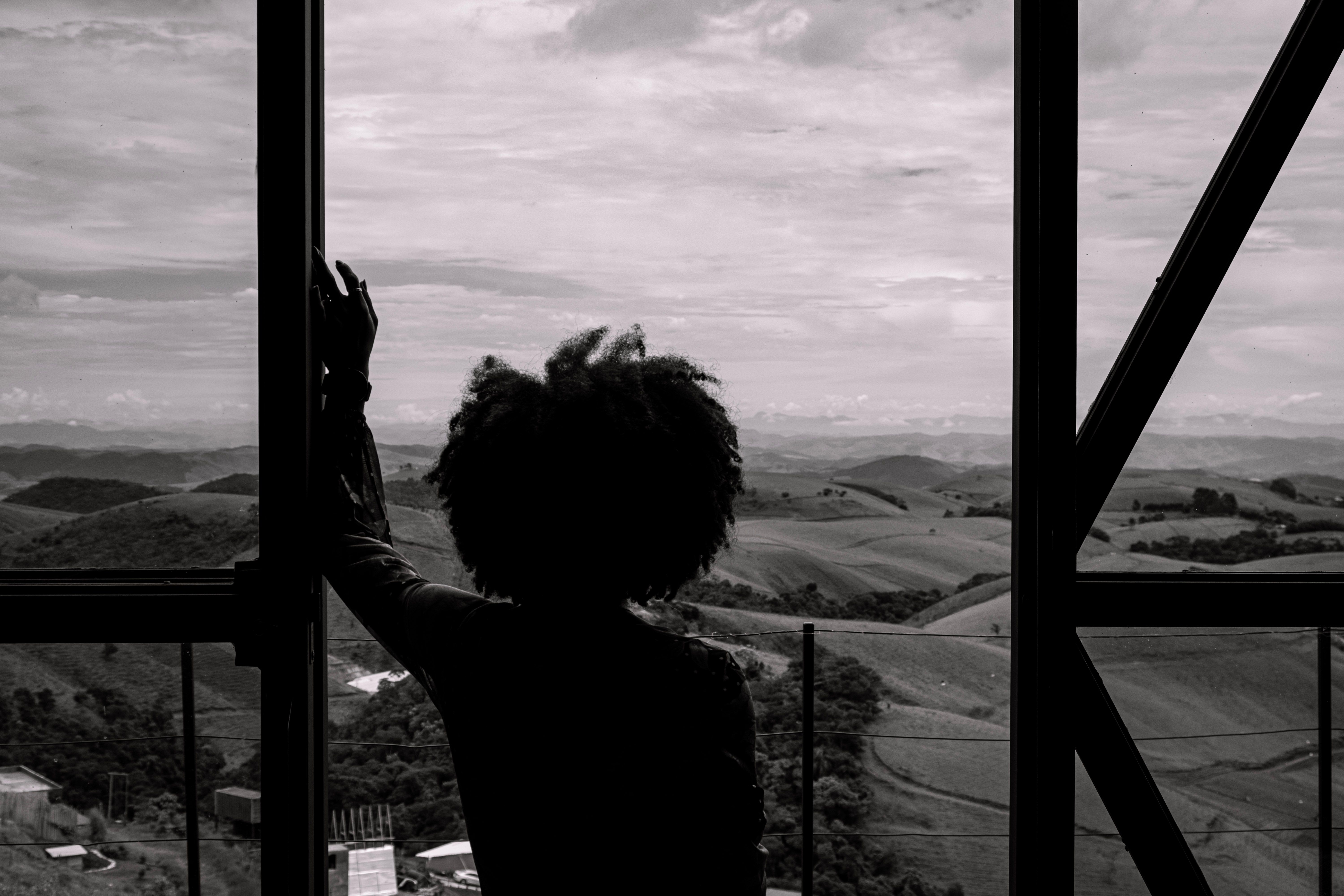Black and white silhouette of a person gazing at scenic Brazilian hills from a window.