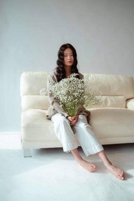 A young woman holding a bouquet of flowers, sitting elegantly on a beige sofa.