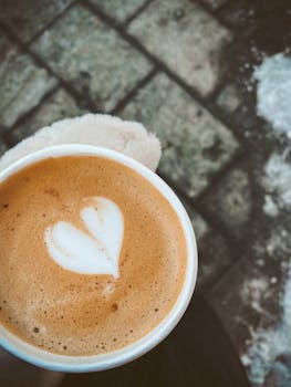 Close-up of heart-shaped latte art in a paper cup on a cold day.