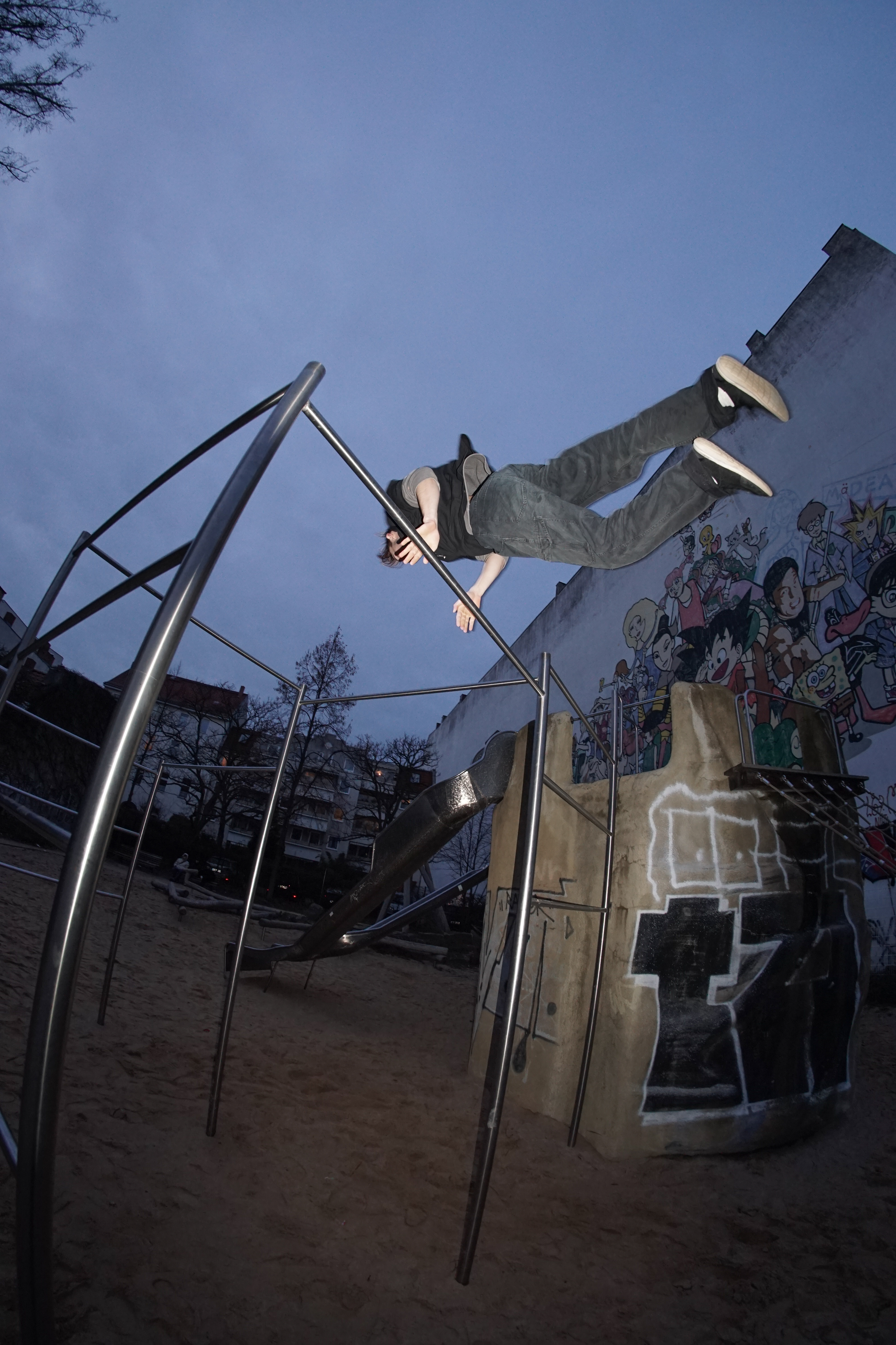 A man performing a calisthenics routine on an outdoor metal bar in Berlin.