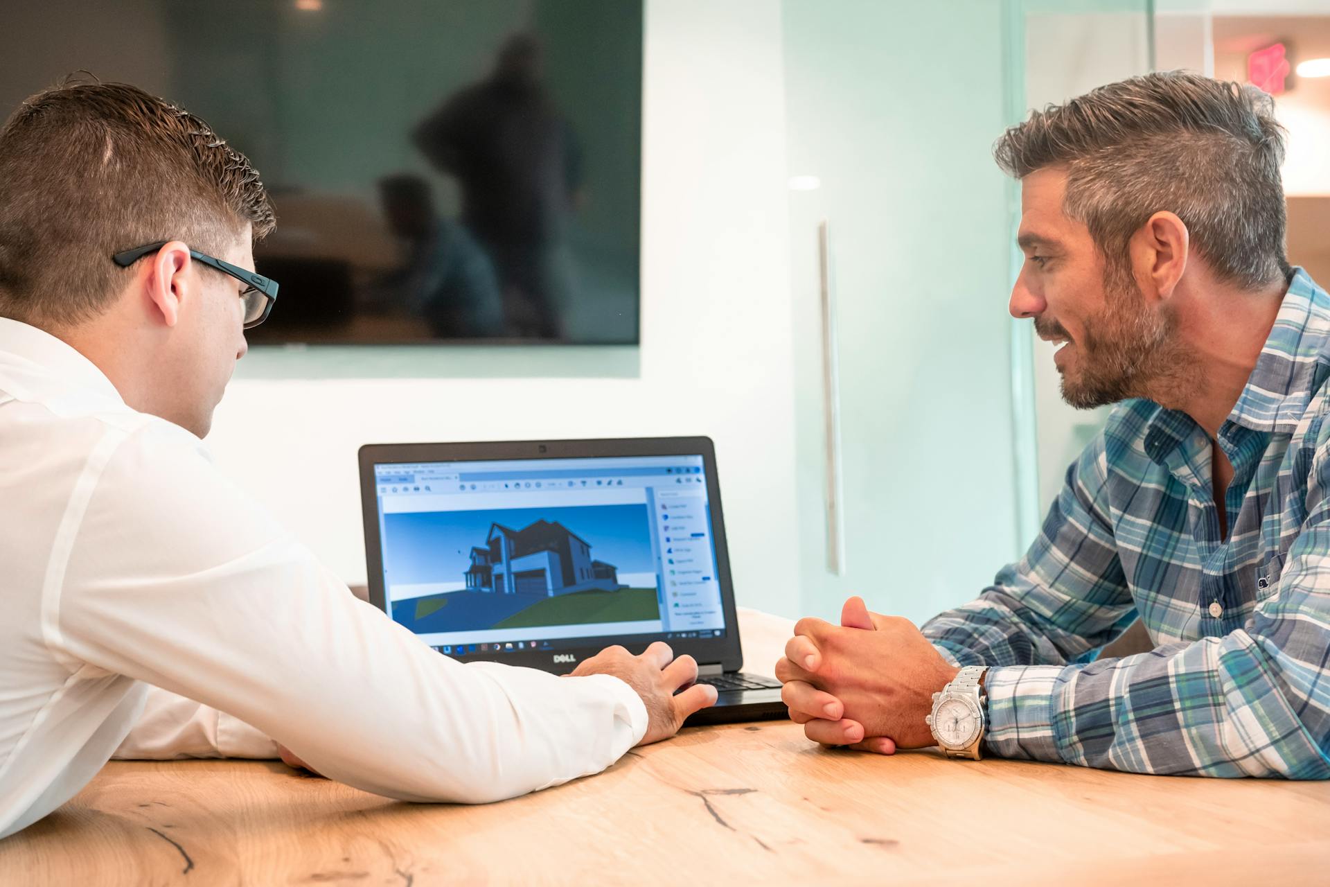 Two professionals discussing a 3D architectural design on a laptop in a modern office.