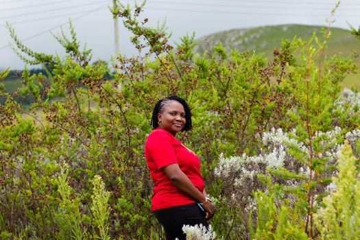 A woman in a red shirt stands amidst lush green shrubs, showcasing natural beauty.