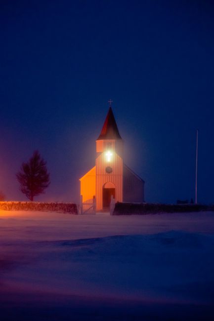 A brightly lit church surrounded by snow under a dark night sky in Reykjavik, Iceland.
