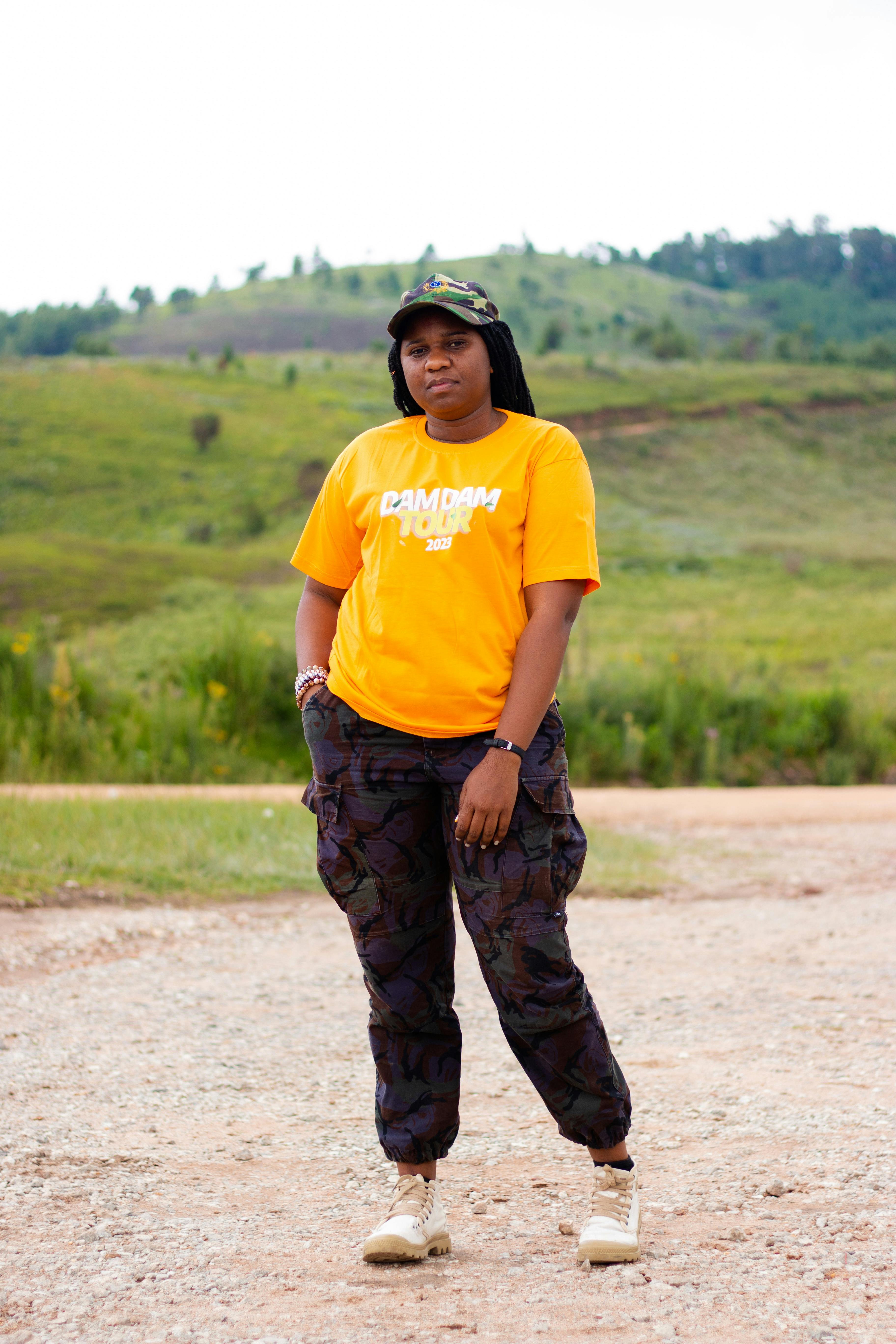 Young woman in bright outfit stands confidently amidst lush countryside, embodying casual rural style.