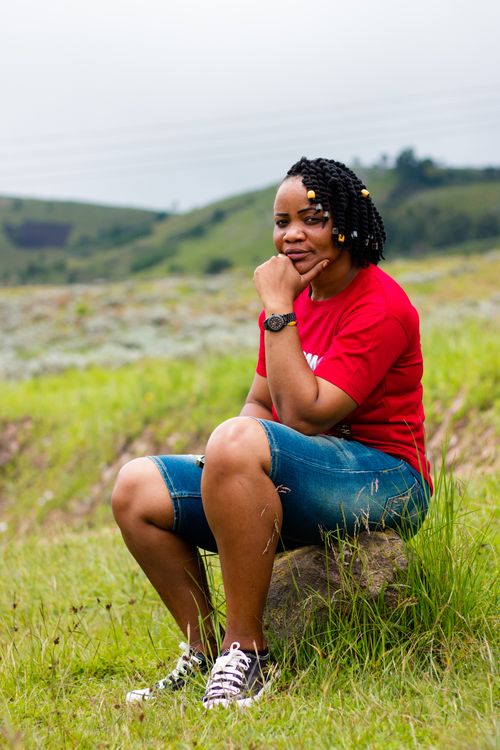 Free Casual portrait of a woman in red t-shirt sitting on a rock in a lush green landscape. Stock Photo