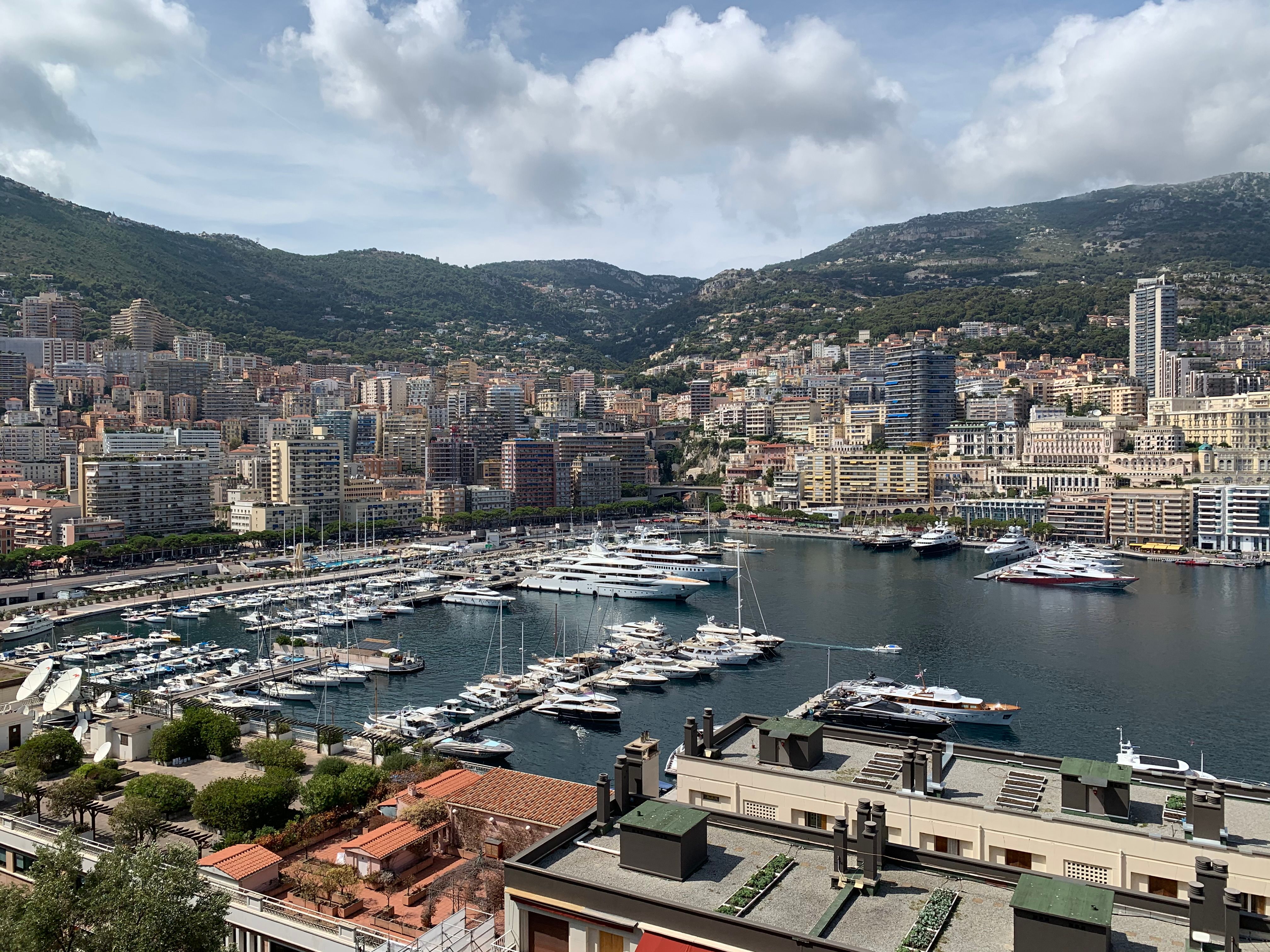 A scenic view of Monaco's harbor filled with yachts surrounded by city buildings and mountains.