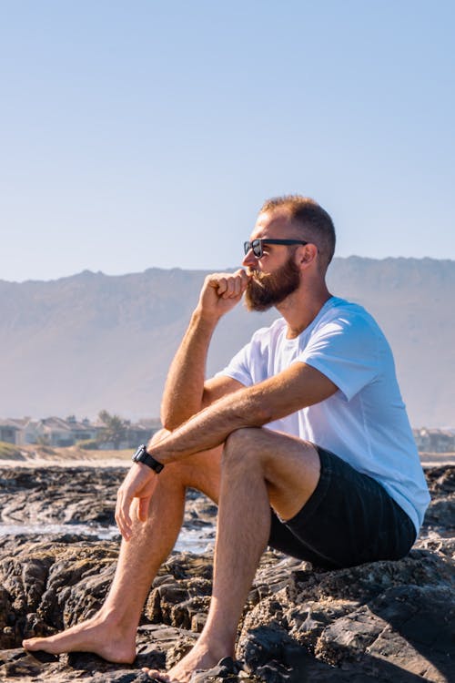 Bearded Man Sitting on a Rocky Beach 