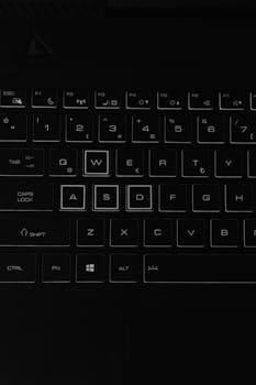 Close-up of a laptop keyboard with illuminated keys in a dark setting, highlighting key details.