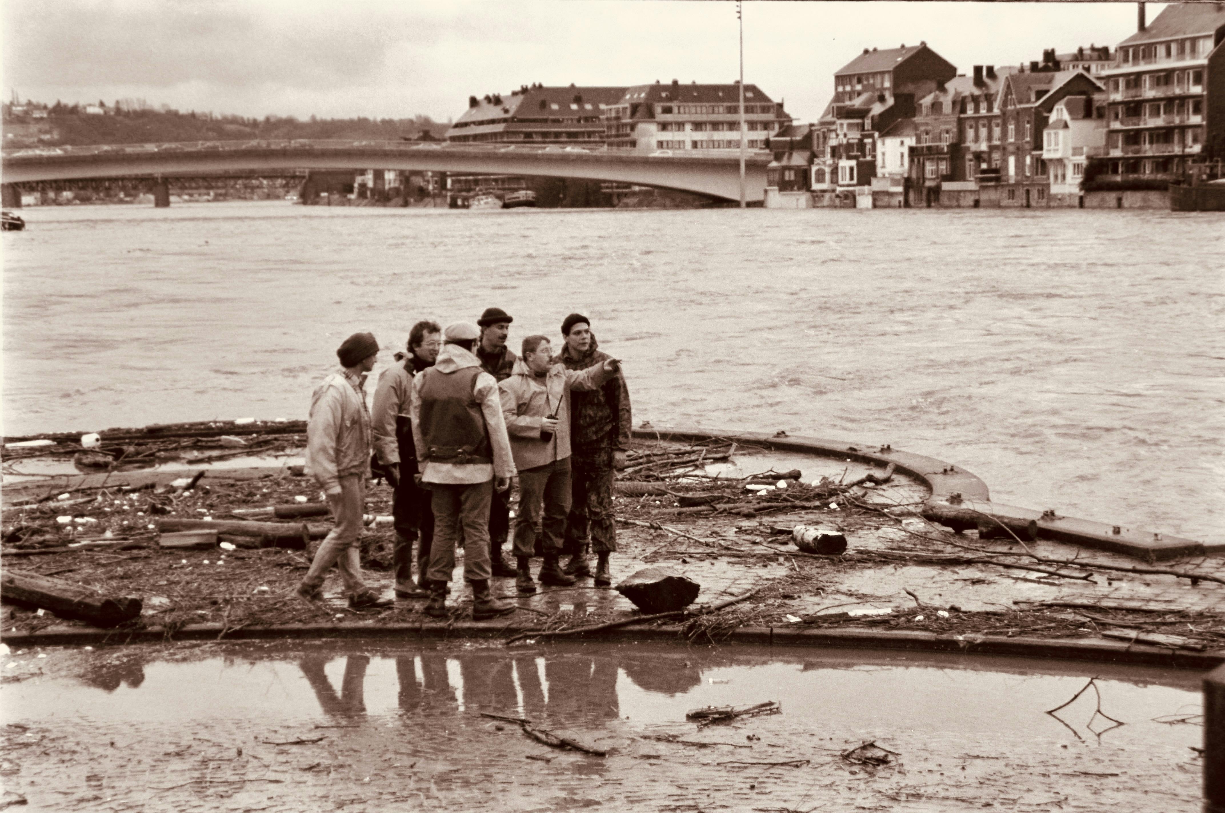 A group of men stands on debris along a river during a flood in a vintage sepia tone.