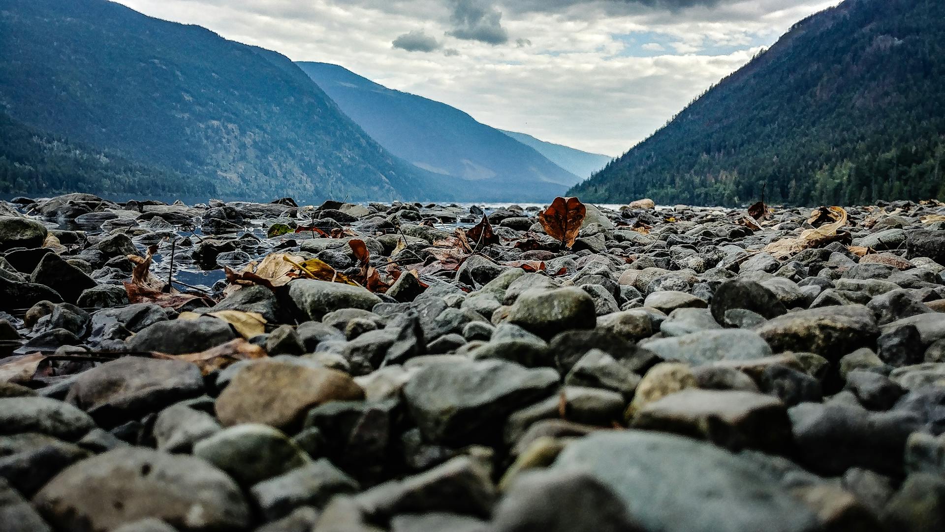 Rocky riverbank in Little Fort, BC offers a serene view of mountains and water.