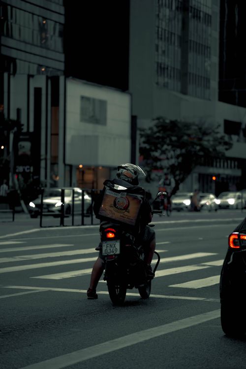 Free A delivery person on a motor scooter navigates city streets at twilight. Stock Photo
