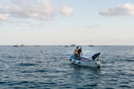 三名男子乘着一艘渔船，在蓝天下平静的水域中航行