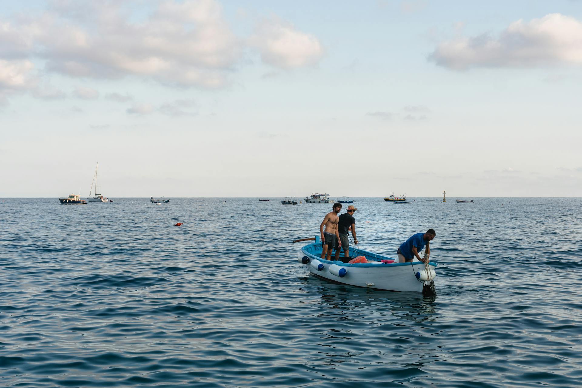 Three men on a fishing boat navigating the calm waters under a blue sky.