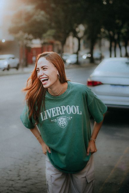 A woman joyfully laughing while wearing a Liverpool t-shirt in an urban outdoor setting.