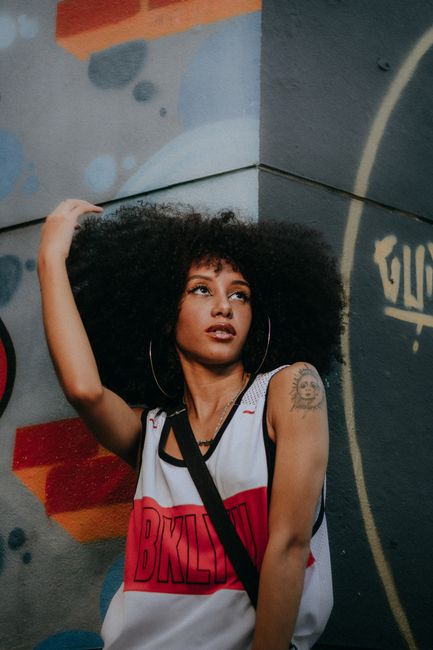 Stylish urban portrait of a young woman with an afro hairstyle against a graffiti wall.
