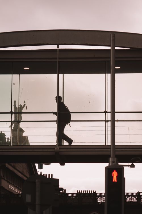 Free Silhouette of a person walking on a glass footbridge in Dublin, Ireland, against an urban backdrop. Stock Photo