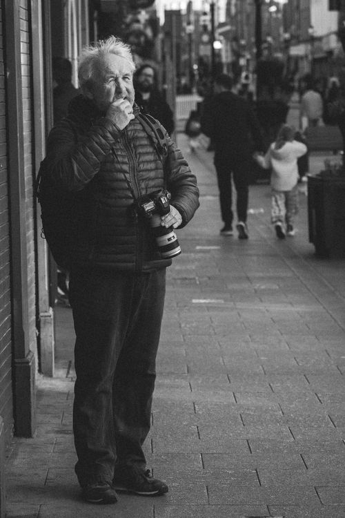 Free Black and white image of an elderly photographer standing on a Dublin sidewalk. Stock Photo
