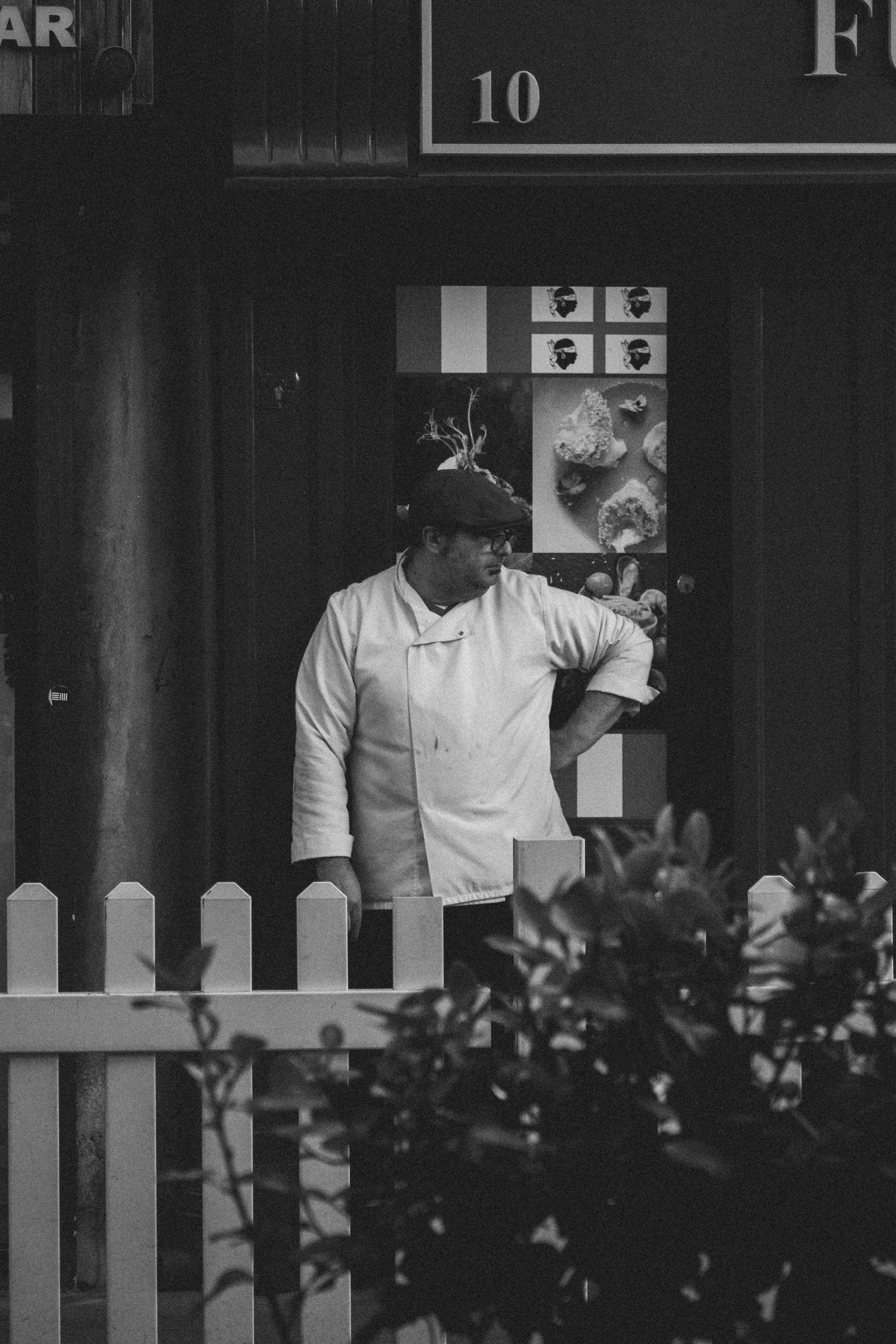 A chef in a white uniform stands outside a restaurant in Dublin. Shot in black and white.