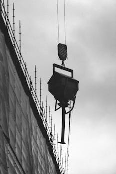 Black and white photo of a crane lifting at a construction site with scaffolding.