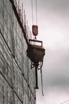 A crane lifting a concrete container at a construction site against a cloudy sky.