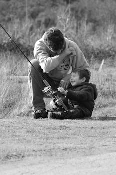 A heartwarming black and white photo of a father teaching his son how to fish in a peaceful outdoor setting.