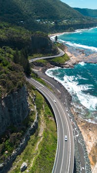 Aerial view of a winding coastal highway along the turquoise sea in Coalcliff, Australia.