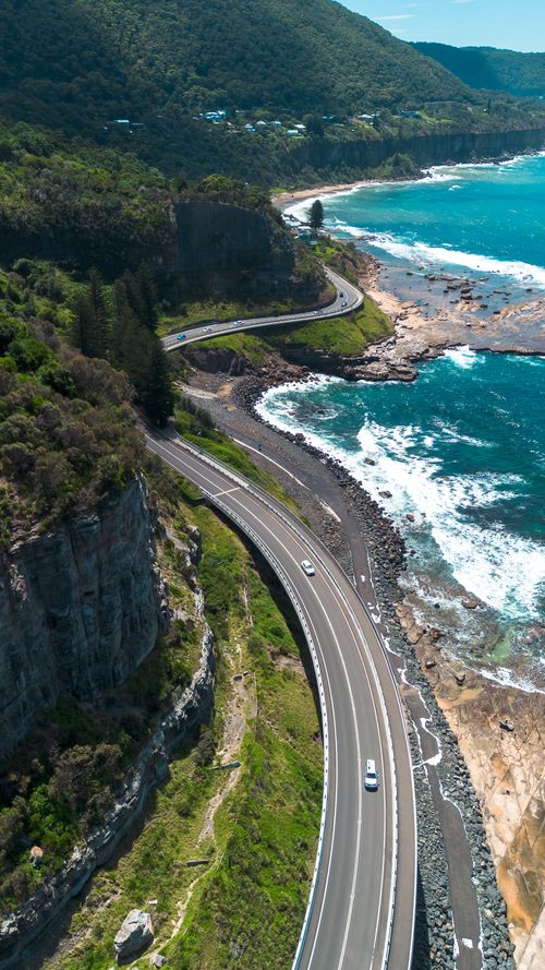 Free Aerial view of a winding coastal highway along the turquoise sea in Coalcliff, Australia. Stock Photo