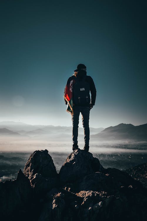 Free Man Carrying Backpack Standing on Rock Formation Stock Photo