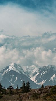 A stunning view of snowcapped mountains with clouds and trees in the foreground.