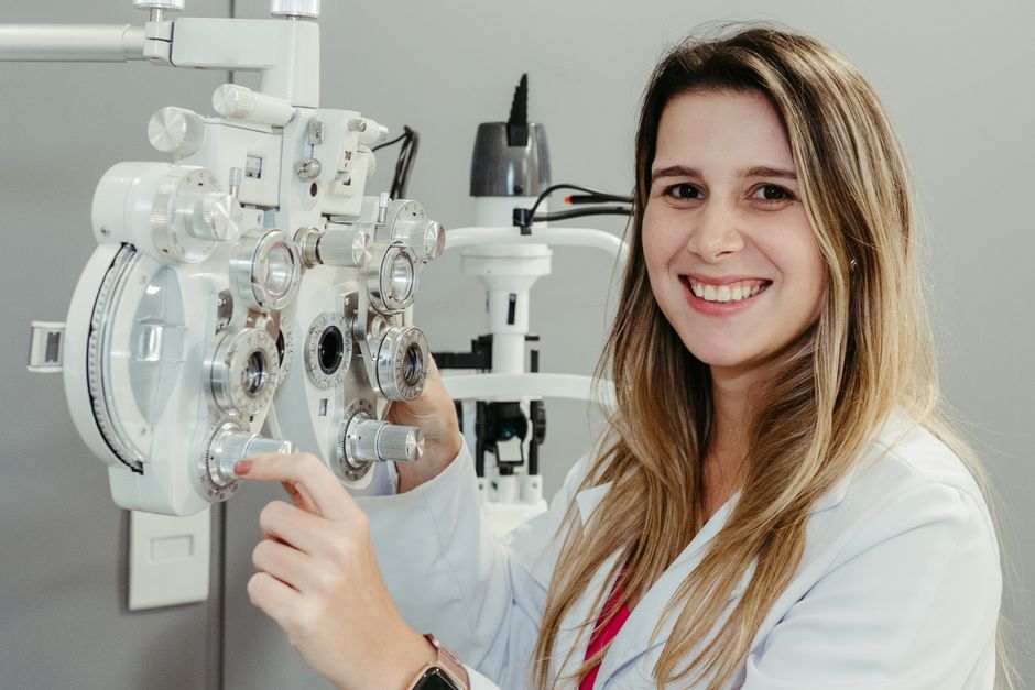 Female optician in white coat smiling while using phoropter. Perfect for healthcare imagery.