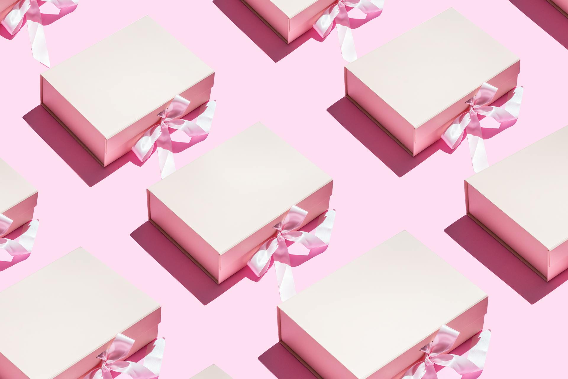 Aesthetic pink gift boxes with ribbons in a seamless pattern on a pink background.