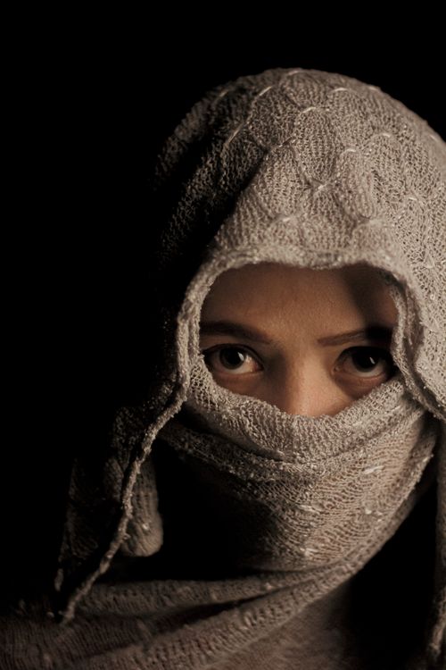 Free Moody portrait of a woman with piercing eyes partially hidden by a grey hijab. Stock Photo