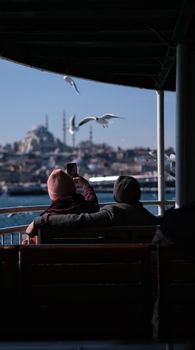 A couple on a ferry takes pictures of seagulls and Hagia Sophia, Istanbul.