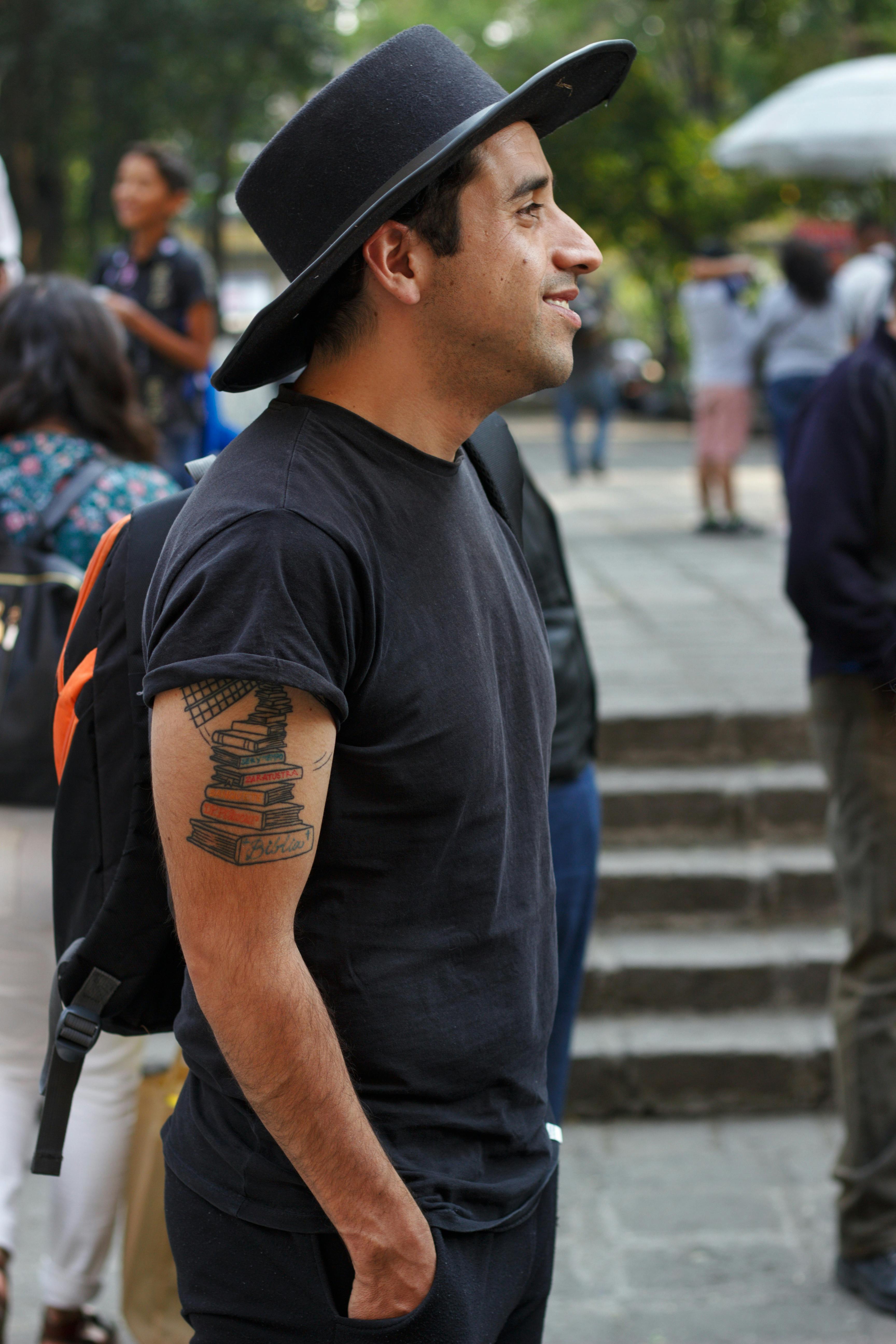 Man in black attire standing outdoors, showcasing a stack of books tattoo.