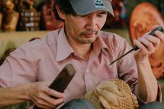Man focused on detailed wood carving in a workshop, surrounded by tools and sculptures.