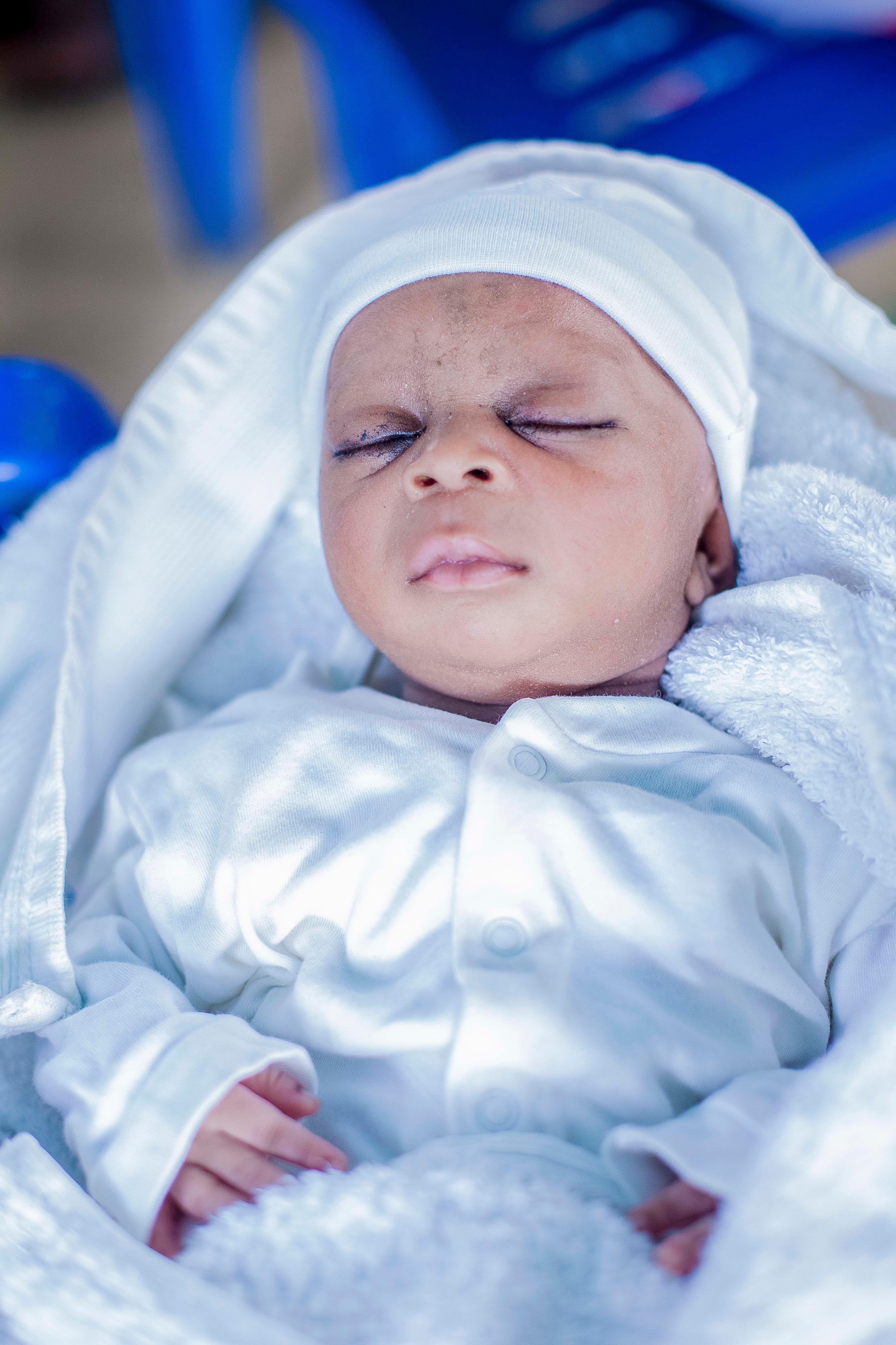 A serene portrait of a baby peacefully sleeping, dressed in a white outfit and hat.