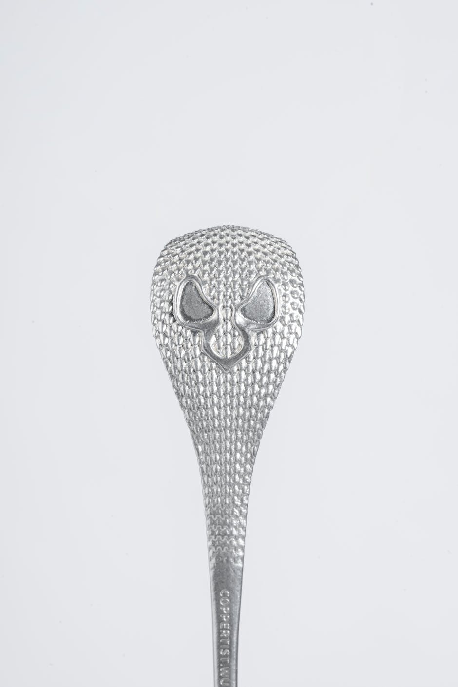 Close-up of a silver textured spoon with a unique design on a white background.