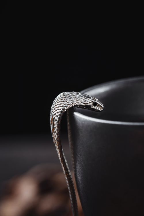 Free A close-up shot of a silver snake draped over a black cup on a dark background. Stock Photo