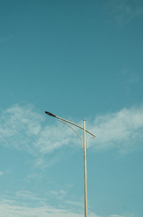 Free A lone streetlight stands against a bright blue sky with fluffy white clouds. Stock Photo