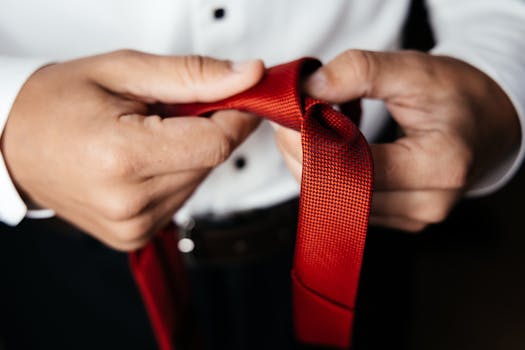Close-up of a man's hands tying a red necktie, showcasing elegance and style.