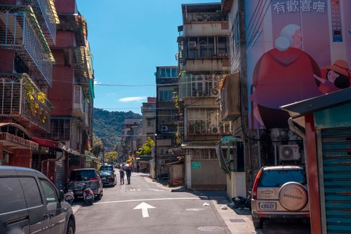 Free Sunny urban street scene with colorful buildings, murals, and parked vehicles under a clear blue sky. Stock Photo